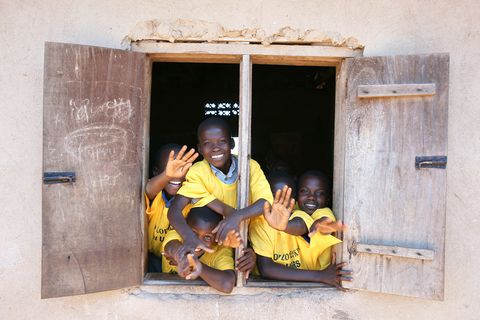children waving from a window in Uganda