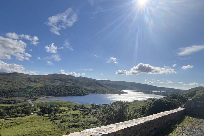 A sunny sky over green, rolling hills and a clear lake in Ireland