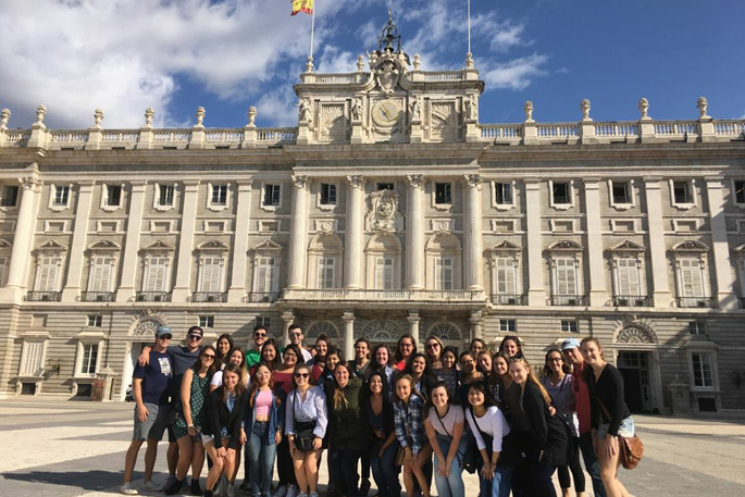 A large group of students poses for a photo in front of the Royal Palace of Madrid in Spain
