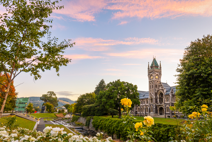A pink and blue sunset over a building at the University of Otago, surrounded by lush green landscape
