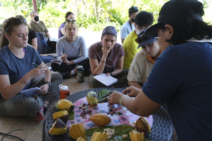 A group of students take notes while an instructor explains different Thai foods