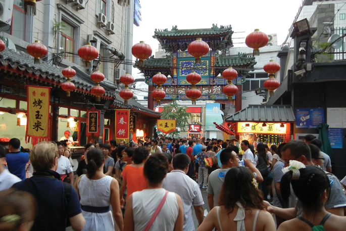 A crowd of people walk the streets in China, with Chinese banners and lanterns surrounding the busy street