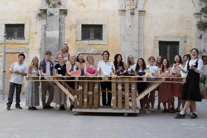A group of students stand behind a waist high outdoor table and pose for the camera