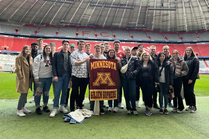 A groups of students hold a Minnesota Gophers flag in a soocer stadium in Germany
