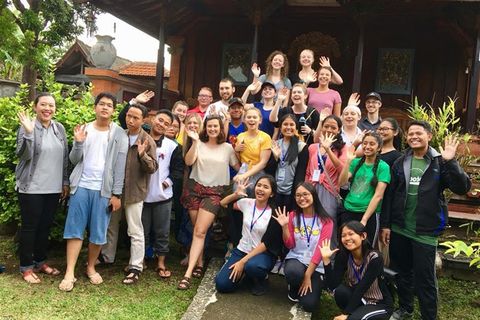 A group of students and Balinese smile and wave for the camera