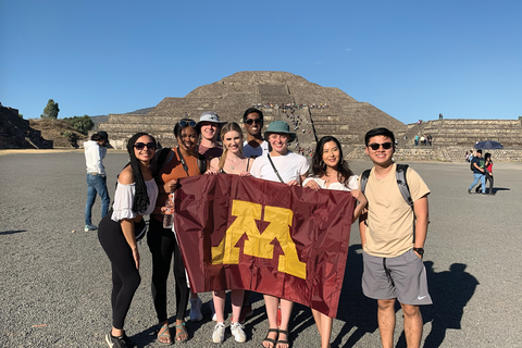 A group of students hold a maroon UofM flag in front of Teotihuacan, Mexico