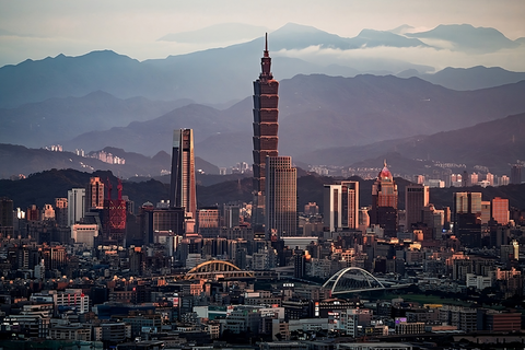A tall skyscraper looms over the city of Taipei, with the mountains covered in clouds in the background