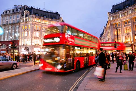 A red double decker bus drives the busy streets of London at sundown
