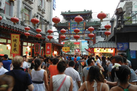 A crowd of people walk the streets in China, with Chinese banners and lanterns surrounding the busy street
