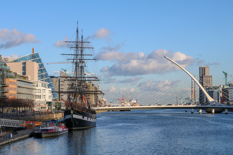A modern, white bridge spans over water in Dublin, Ireland. Buildings stand on either side of the water while an historic ship sits on the water.