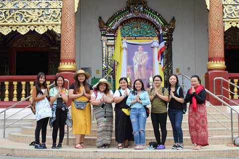 A group of students stand in front of a painting of a Thai king, their palms pressed together in the traditional Thai greeting