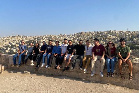 A group of students sit on a wall in Jordan, witht he city of Amman behind