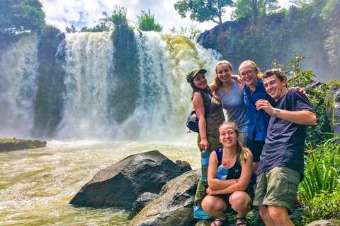 Students stand on a rock in front of three waterfalls