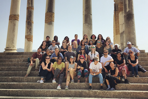 A group of students sit for a photo on the steps in front of ancient columns